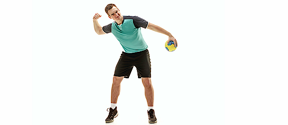 Ein Handballspieler in einem türkisfarbenen Trikot hält einen Handball in seiner linken Hand. Er macht mit der rechten Hand eine Faust und freut sich über einen guten Spielzug.