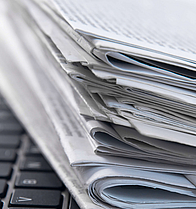 Stapel Zeitungen liegt auf der Tastatur eines geöffneten Laptops