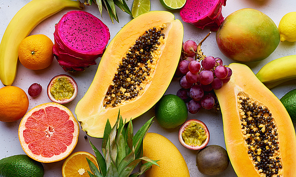 Tropisches Fruchtmuster mit Mango, Papaya, Pitahaya, Passionsfrucht, Trauben, Limetten und Ananas. Tisch mit Zutaten für Sommersnacks auf betoniertem Hintergrund. Bio-gesunde Nachspeise