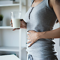 Frau hält mit der rechten Hand die Milch und mit der linken ihren Bauch.