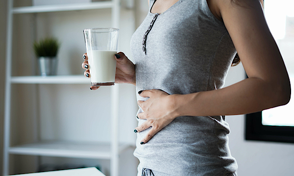 Frau hält mit der rechten Hand die Milch und mit der linken ihren Bauch.