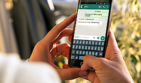 Nahaufnahme eines Handys, auf dem ein WhatsApp Chat geöffnet ist. Das Handy wird von zwei Händen gehalten.