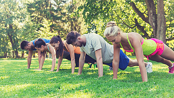 Eine Gruppe von Sportlern macht draußen Sport. Sie machen Liegestütz.