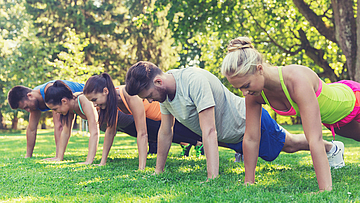 Eine Gruppe von Sportlern macht draußen Sport. Sie machen Liegestütz.