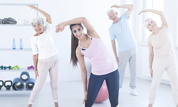 Eine Gruppe Senioren macht Gymnastik mit einer jungen Trainerin. Sie machen Stretching.