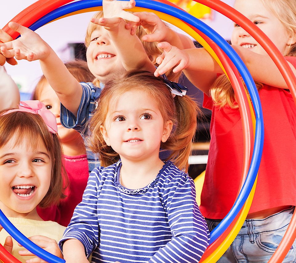 Fröhliche Kinder sind beim Sport und schauen gemeinsam durch einen Reifen.