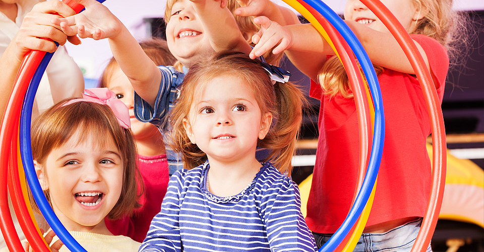 Fröhliche Kinder sind beim Sport und schauen gemeinsam durch einen Reifen.