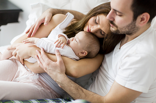 Junge Familie mit Baby liegen gemeinsam im Bett.