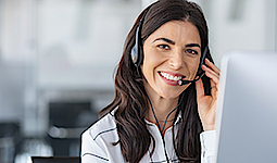 Frau mit Headset arbeitet in einem modernen Büro, sie ist im Gespräch mit einem Kunden.