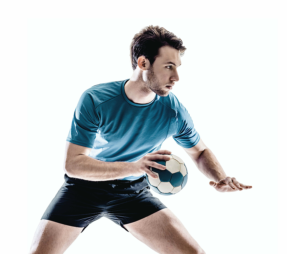 Ein Handballspieler in einem blauen Trikot hält den Handball in der rechten Hand. Er sucht sich einen Spieler, zu dem er den Ball werfen kann.