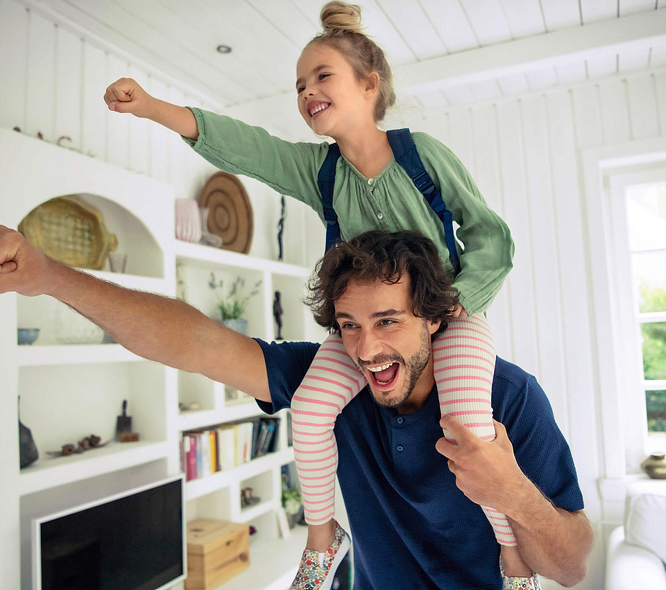 Vater trägt seine Tochter huckepack, beide strecken einen Arm mit einer Faust nach vorne.