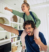 Vater trägt seine Tochter huckepack, beide strecken einen Arm mit einer Faust nach vorne.