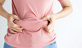 Eine junge Frau greift mit beiden Händen an ihren Bauch und zeigt ihr Bauchfett.