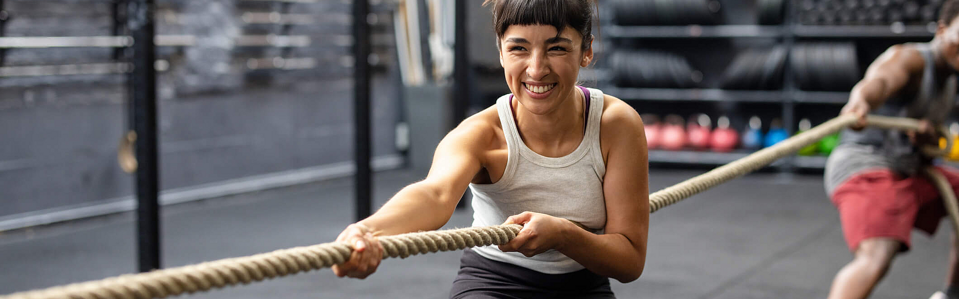 Eine Frau macht im Fitnessstudio Tauziehen und lacht dabei