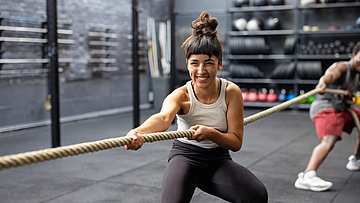 Eine Frau macht im Fitnessstudio Tauziehen und lacht dabei