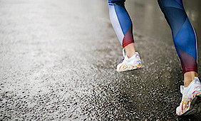 Eine Läuferin rennt in einer bunten Laufhose über den nassen Asphalt.