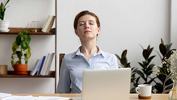 Eine Frau sitzt in einem Büro am Schreibtisch und macht Atemübungen.