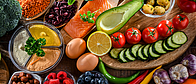 Lebensmittel, die zu einer ausgewogenen Ernährung gehören, wie Gemüse, Lachs, Nüsse, Eier stehen auf einem braunen Untergrund. 