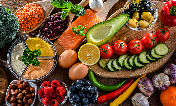 Lebensmittel, die zu einer ausgewogenen Ernährung gehören, wie Gemüse, Lachs, Nüsse, Eier stehen auf einem braunen Untergrund. 