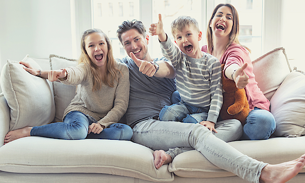 Eine Familie sitzt auf dem Sofa. Sie freuen sich. Die Daumen haben alle erhoben.