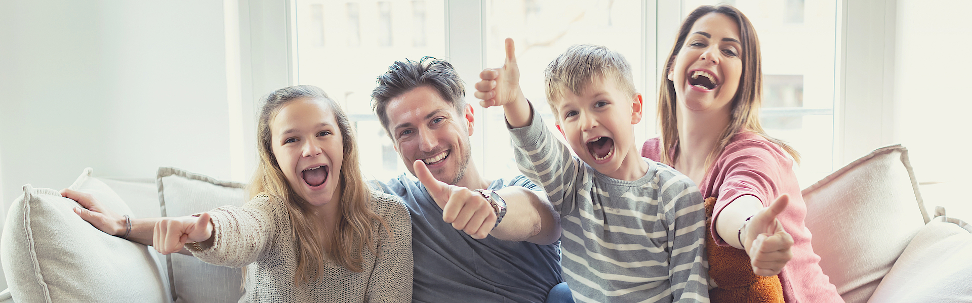 Eine Familie sitzt auf dem Sofa. Sie freuen sich. Die Daumen haben alle erhoben.