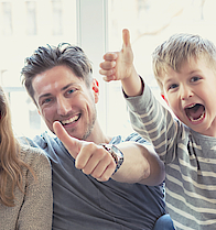 Eine Familie sitzt auf dem Sofa. Sie freuen sich. Die Daumen haben alle erhoben.