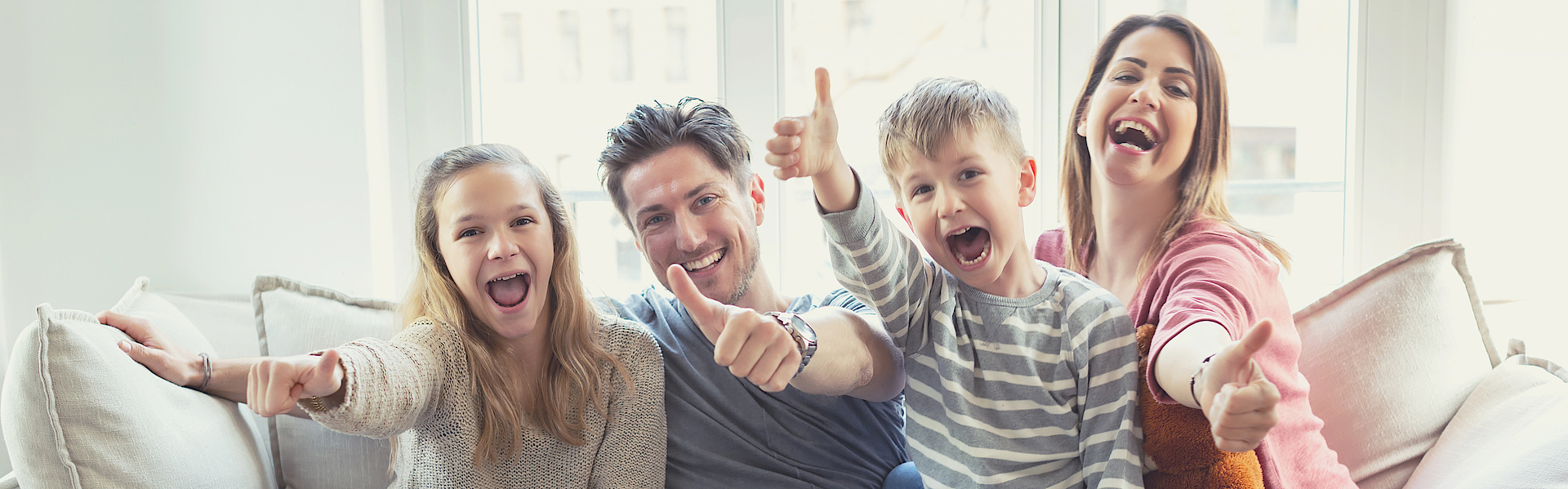 Eine Familie sitzt auf dem Sofa. Sie freuen sich. Die Daumen haben alle erhoben.