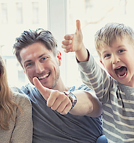 Eine Familie sitzt auf dem Sofa. Sie freuen sich. Die Daumen haben alle erhoben.