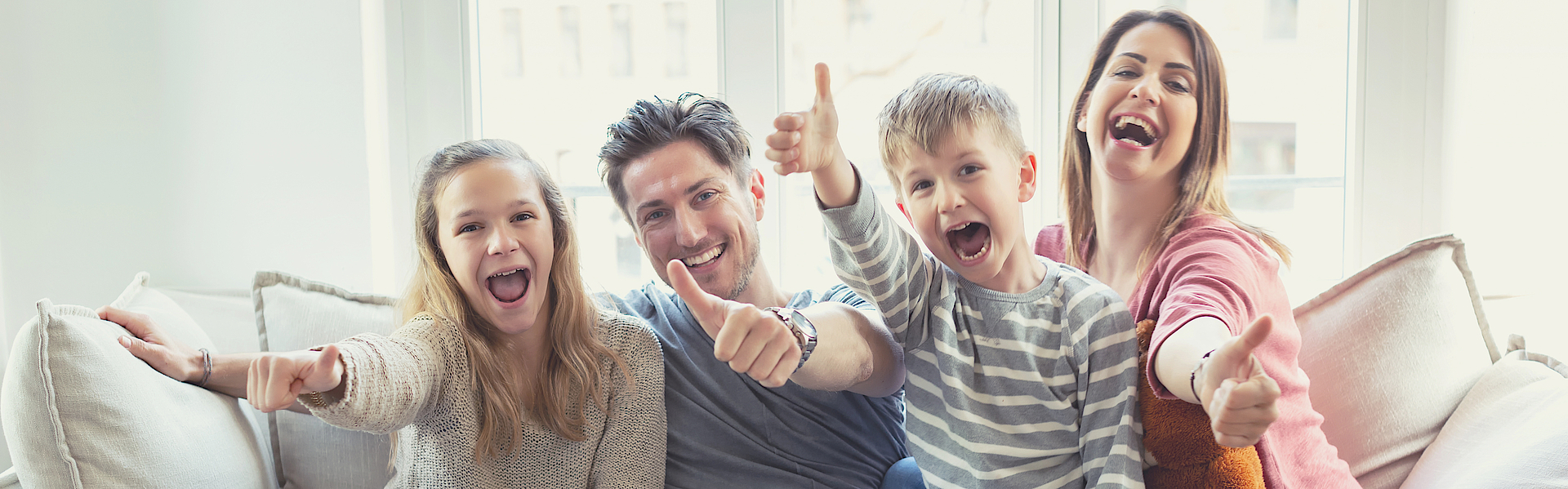 Eine Familie sitzt auf dem Sofa. Sie freuen sich. Die Daumen haben alle erhoben.