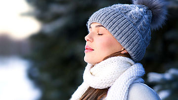 Eine junge Frau steht im Winter im Freien und holt tief Luft.