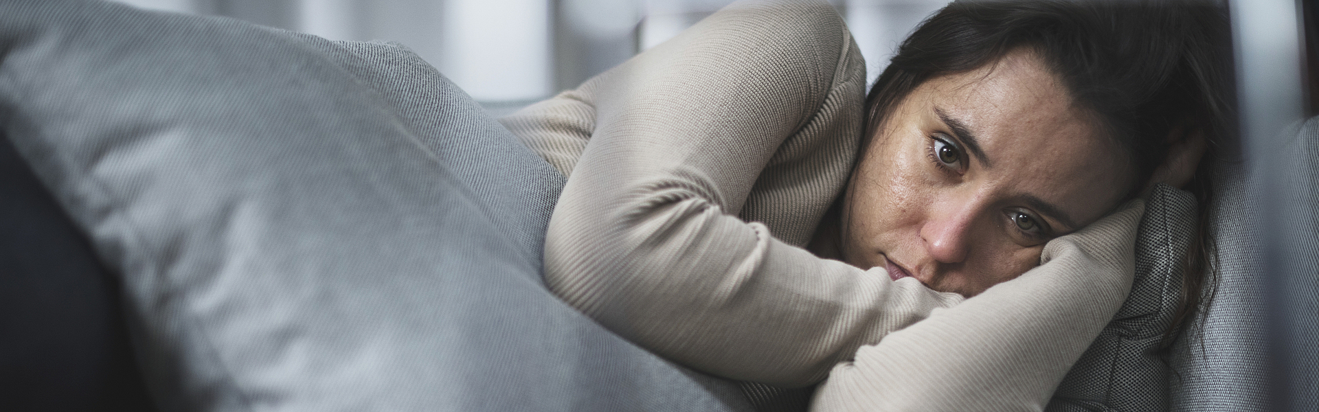 Junge Frau liegt traurig auf einem Sofa.