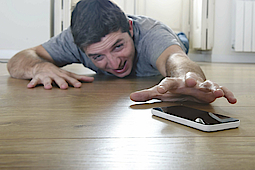 Ein junger Mann liegt am Boden. Vor ihm sein Handy. Er greift ganz verzweifelt danach.