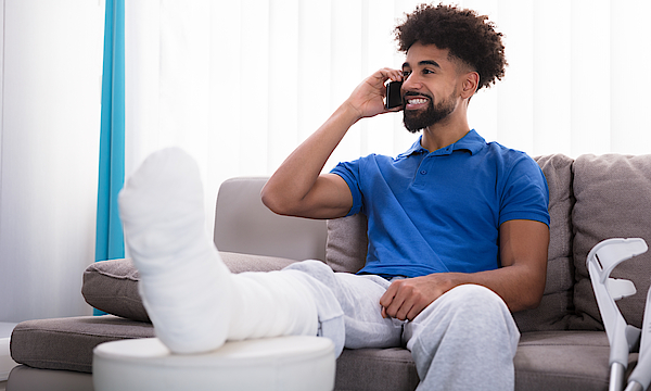 Ein Mann mit einem gebrochenen Bein sitzt auf einem Sofa und telefoniert.