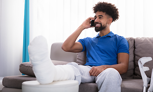 Ein Mann mit einem gebrochenen Bein sitzt auf einem Sofa und telefoniert.