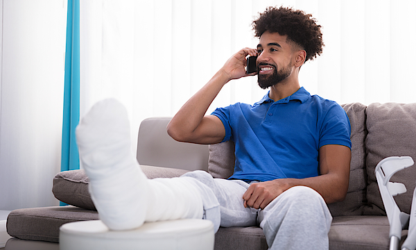 Ein Mann mit einem gebrochenen Bein sitzt auf einem Sofa und telefoniert.