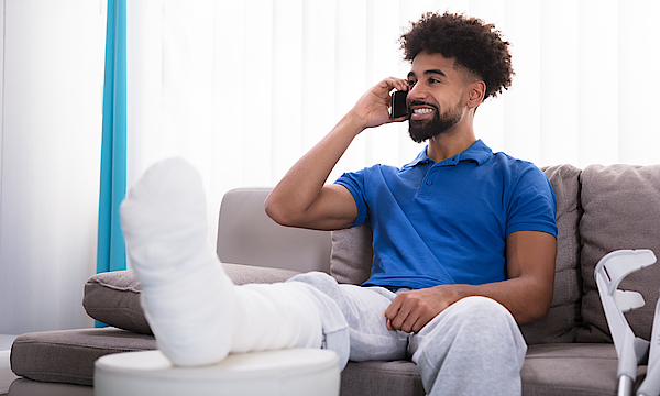 Ein Mann mit einem gebrochenen Bein sitzt auf einem Sofa und telefoniert.