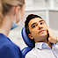 Mann mit Zahnschmerzen liegt auf dem Behandlungsstuhl seines Zahnarztes. Er hält sich die linke Backe.