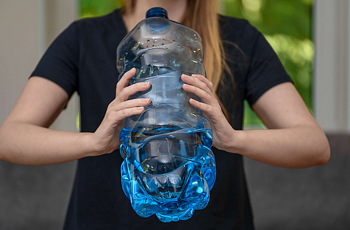 Frau trinkt aus einer sehr großen Falsche Wasser, sie muss die Flasche mit zwei Händen halten.
