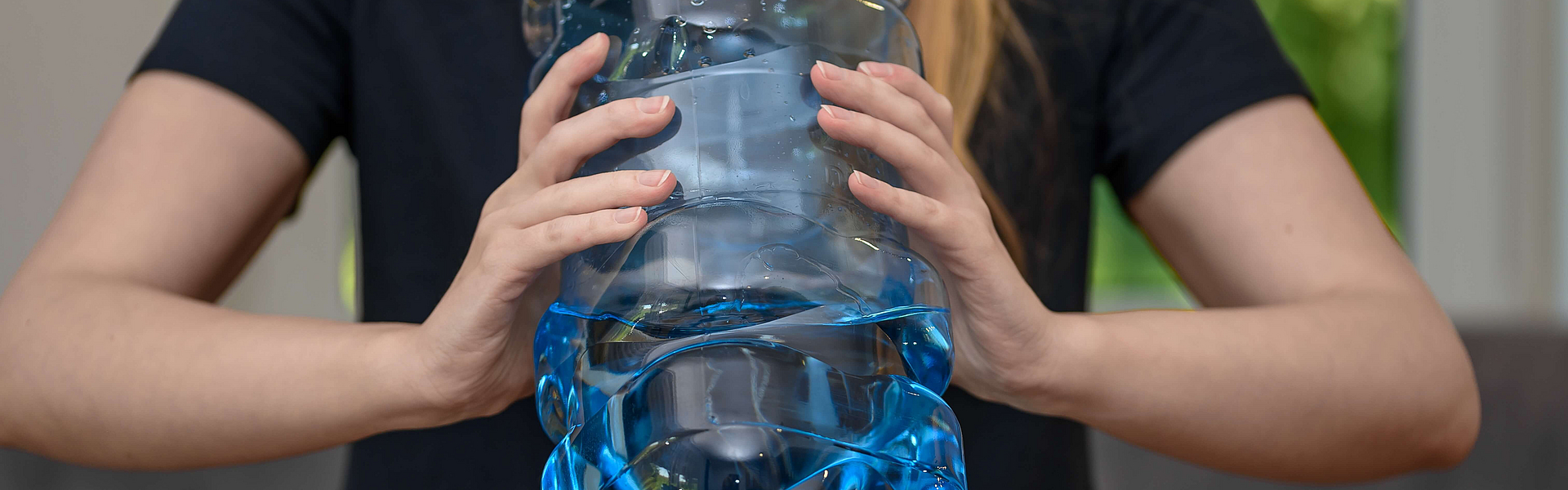 Frau trinkt aus einer sehr großen Falsche Wasser, sie muss die Flasche mit zwei Händen halten.