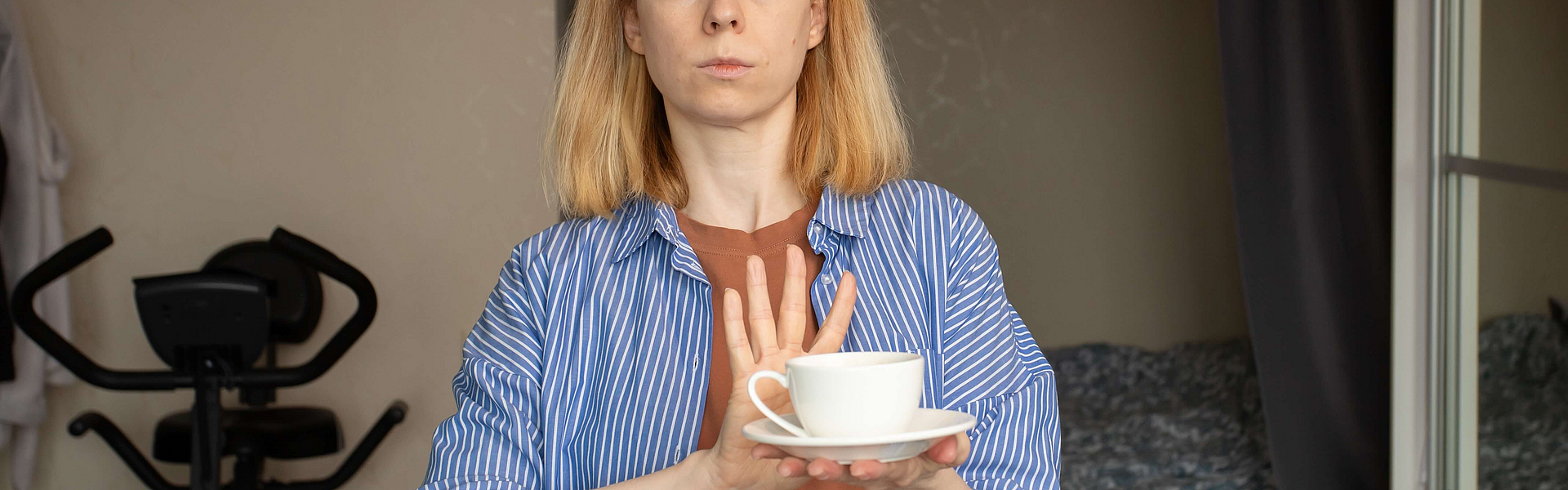 Schwangere Frau hält eine Tasse Kaffee in der Hand und macht mit der anderen Hand eine streckt die andere Hand der Tasse ablehnend entgegen.