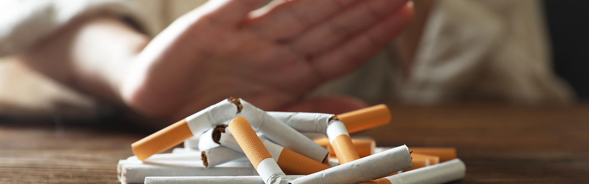 Frau Frau macht Stoppgeste, auf einem Holztisch liegen Zigaretten, die Frau macht einen Nikotinentzug