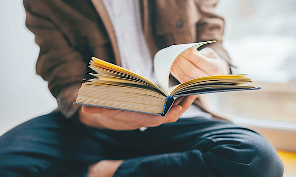 Ein Mann sitzt auf dem Boden. Er liest ein Buch.