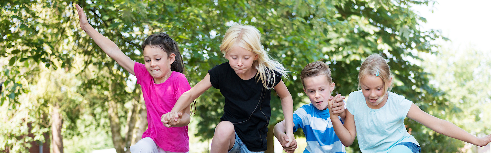 Kinder im Wald hüpfen über einen Baumstamm.