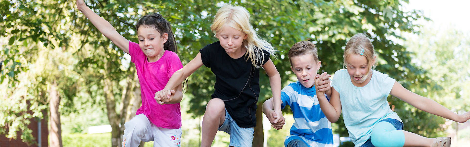 Kinder im Wald hüpfen über einen Baumstamm.