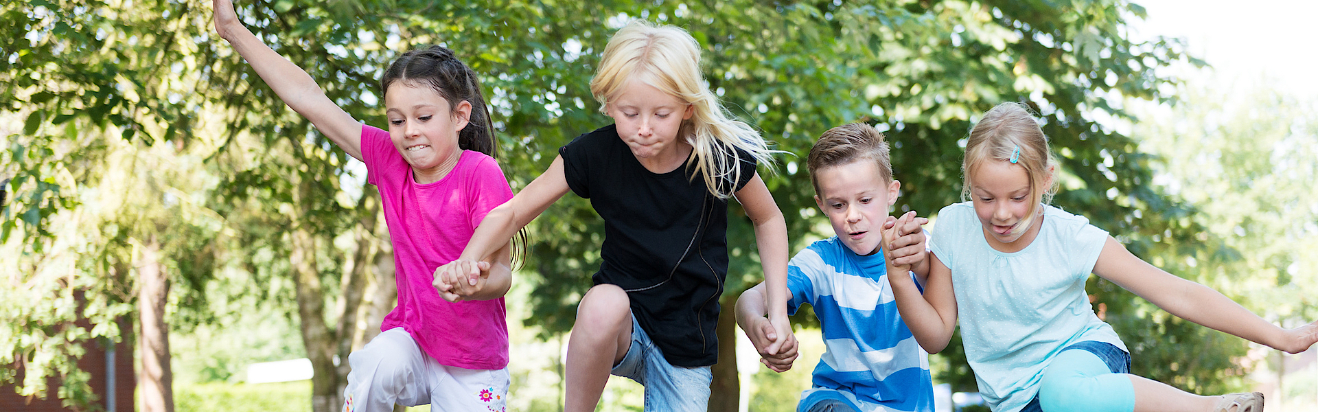 Kinder im Wald hüpfen über einen Baumstamm.