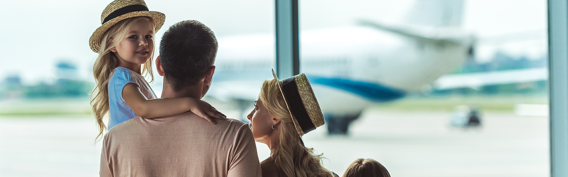 Eine Familie ist im Flughafen und schaut aus dem Fenster auf ein Flugzeug.