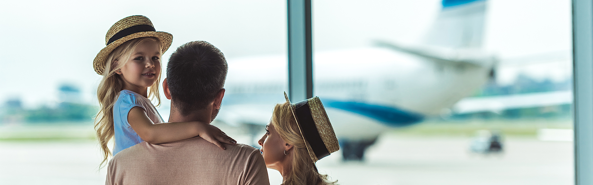 Eine Familie ist im Flughafen und schaut aus dem Fenster auf ein Flugzeug.