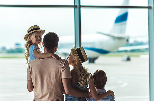 Eine Familie ist im Flughafen und schaut aus dem Fenster auf ein Flugzeug.