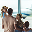 Eine Familie ist im Flughafen und schaut aus dem Fenster auf ein Flugzeug.