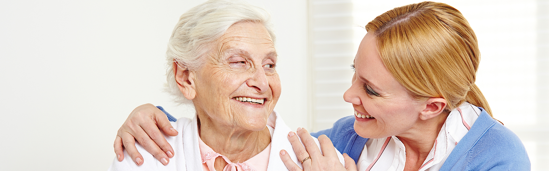 Lachende Seniorin schaut ihre Tochter an.